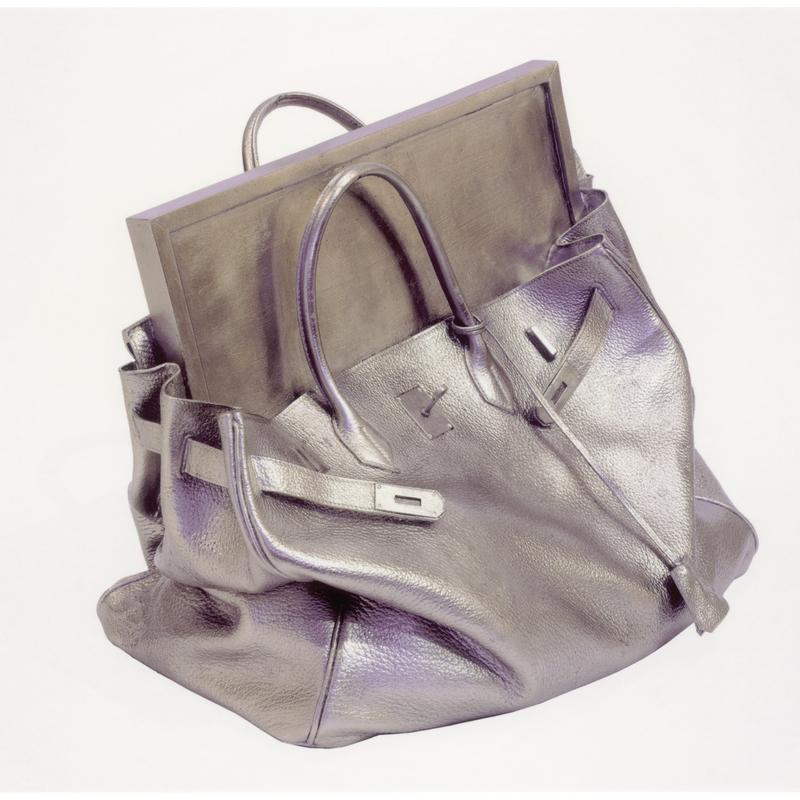 Silberne Handtasche mit einem rechteckigen, silbernen Objekt darin, auf weißem Hintergrund.