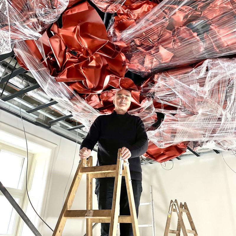 Mann auf einer Holzleiter in einem Raum mit rotem Deckenrelief.