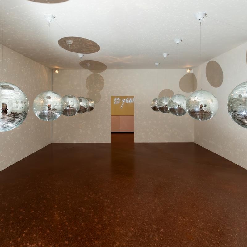 Spiegelkugeln hängen von der Decke in einem Raum mit braunem Boden und projizierten Lichtmustern an den Wänden.