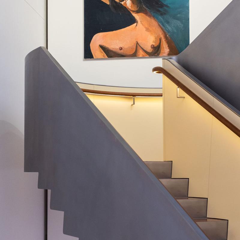 Treppenaufgang mit grauen Stufen und einem bunten Gemälde einer figurativen Darstellung an der Wand.