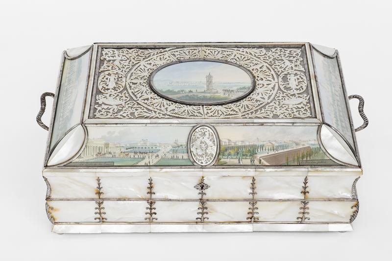 Diese Schatulle wurde um das Jahr 1825 gemacht.
Die Aquarelle auf der Schatulle wurden von Balthasar Wigand gemalt.

Die Schatulle ist aus Perlmutt und Silber.
Sie sieht edel und kostbar aus.
An den Seiten hat sie kleine Henkel, mit denen man sie tragen kann.

Auf dem Deckel sieht man in der Mitte ein kleines Bild:
Es zeigt die Spinnerin am Kreuz – ein bekannter Ort in Wien.
Im Hintergrund sieht man die Stadt Wien und Menschen auf Pferden.

Rund um das Bild ist ein feines Muster aus Metall, mit Blättern und Figuren.
Auch an den Seiten der Schatulle sind gemalte Szenen von Wien zu sehen:
nämlich das äußere Burgtor mit Heldenplatz.