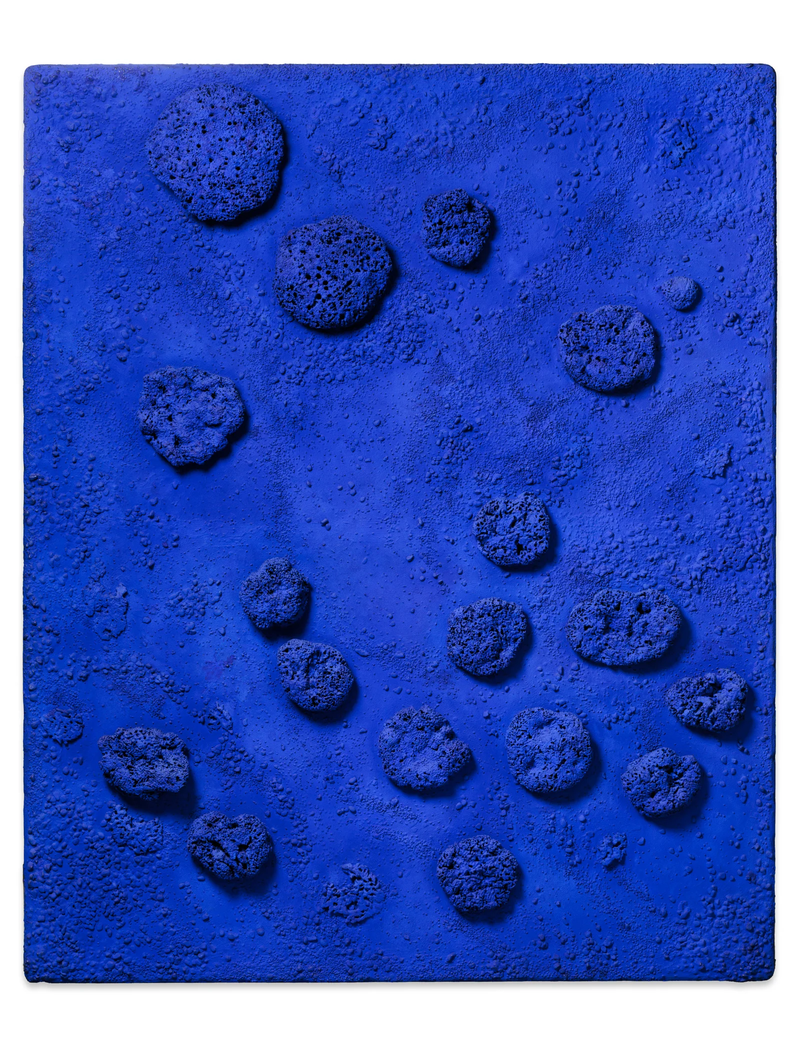 Das Kunstwerk ist ein rechteckiges Relief – also eine Art Bild mit dreidimensionalen Formen. Es ist ganz in intensivem Ultramarinblau gehalten, einer Farbe, die Yves Klein berühmt gemacht hat. Diese Farbe wirkt leuchtend, tief und fast körperlich – als würde sie Licht in sich aufnehmen.

Auf der Fläche sind echte Naturschwämme und kleine Kieselsteine befestigt. Sie sind unregelmäßig verteilt und ragen aus der Oberfläche heraus. Manche sind rundlich, andere eher flach oder porös. Die Schwämme werfen feine Schatten, je nach Lichteinfall – das gibt dem Werk eine lebendige, bewegte Struktur.

Die Fläche selbst ist nicht glatt, sondern leicht körnig und rau. Auch dort sieht man kleinere Erhebungen, die wirken, als hätte sich die Farbe natürlich über den Untergrund gelegt, wie Sand, der sich am Meeresboden sammelt.

Die Schwämme sind vollständig mit Yves Kleins spezieller blauer Farbe getränkt – sie sehen fast wie kleine Himmelskörper oder Tiefseetiere aus. Obwohl das Werk keine Figur zeigt, wirkt es organisch und lebendig.