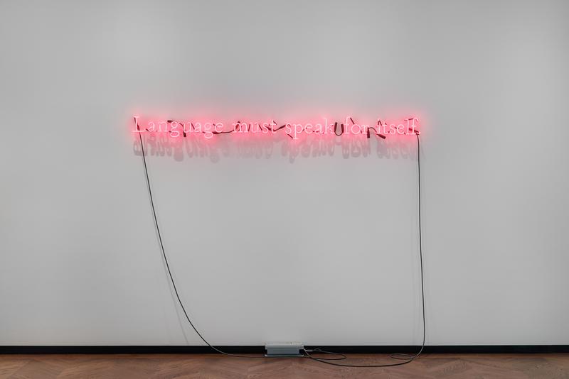 Neoninstallation mit der Aufschrift „Language must speak for itself“ an einer weißen Wand.