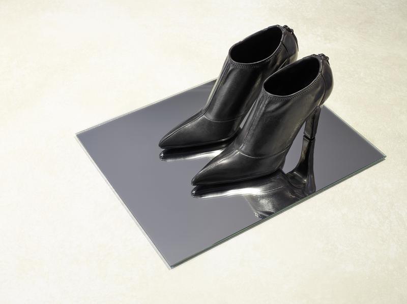 Schwarze High Heels mit spitzen Zehen auf einem spiegelnden Untergrund.