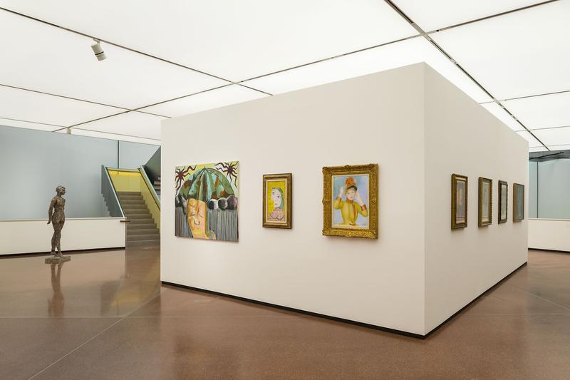 Moderne Galerie mit weißen Wänden, Skulptur und mehreren Gemälden in goldenen Rahmen. Treppe im Hintergrund.
