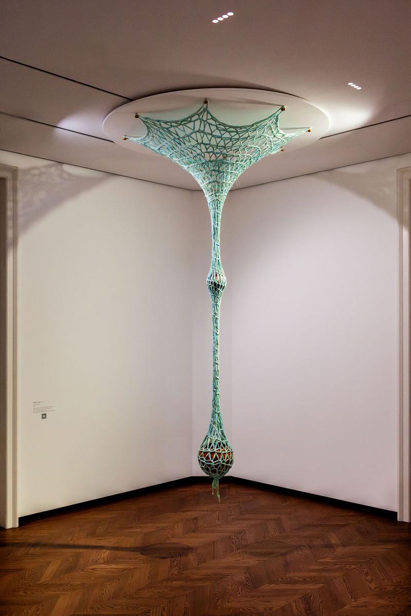 Hängende, netzartige Skulptur in mintgrün, die von der Decke in eine Ecke des Raumes reicht. Holzfußboden im Hintergrund.