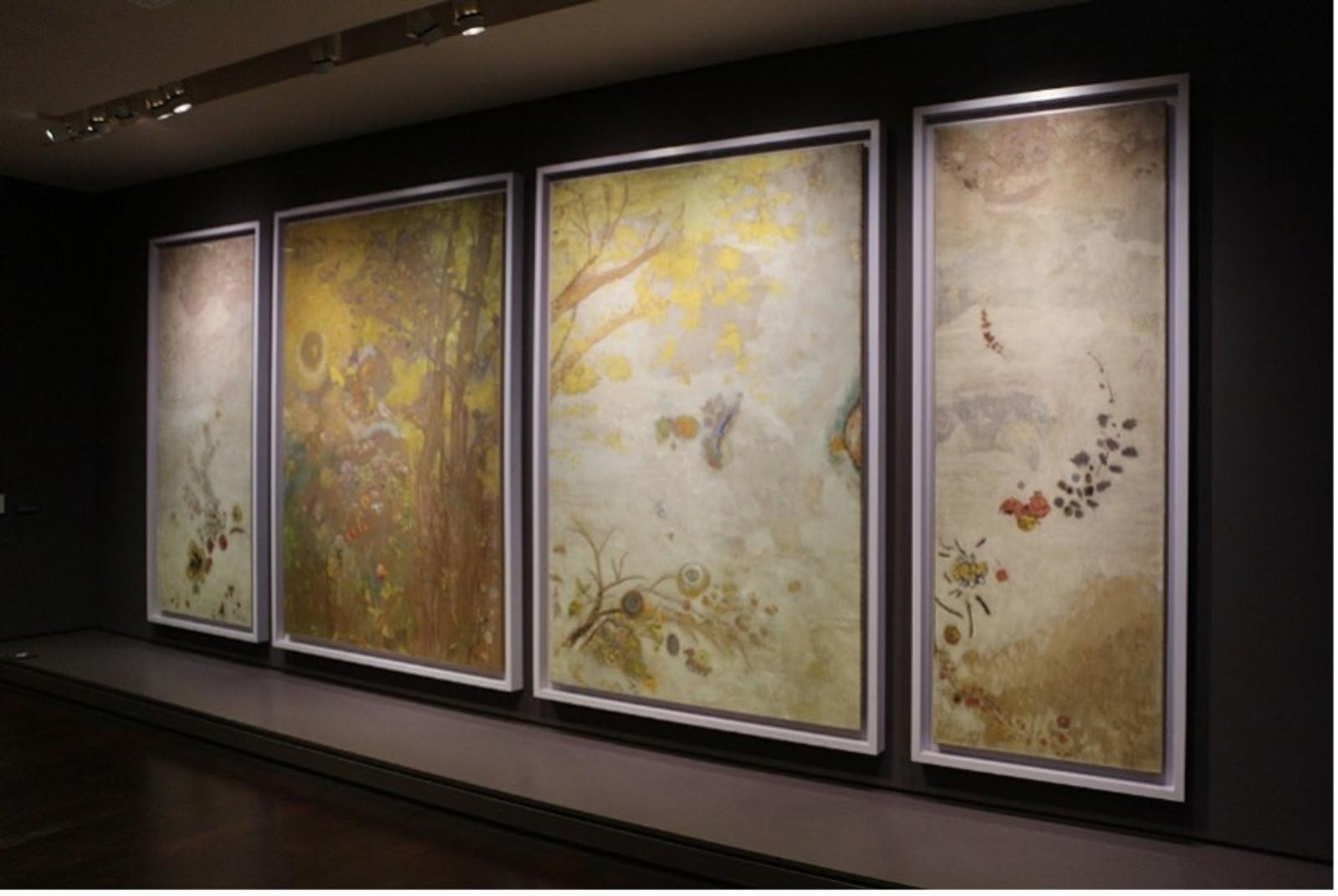 Vier große, gerahmte Gemälde in sanften Farben, hängen an einer dunklen Wand im Musée d'Orsay.