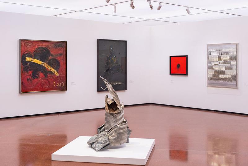 Moderne Kunstgalerie mit abstrakten Gemälden und einer skulpturalen Metallarbeit im Vordergrund.