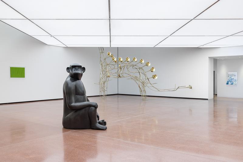 Schwarze Skulptur eines sitzenden Affen in einem modernen Ausstellungsraum mit Kunstwerken.