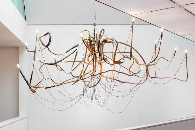 Moderne, kunstvolle Deckenleuchte mit geschwungenen Metallarmen und mehreren Glühbirnen, schwebend im Raum.