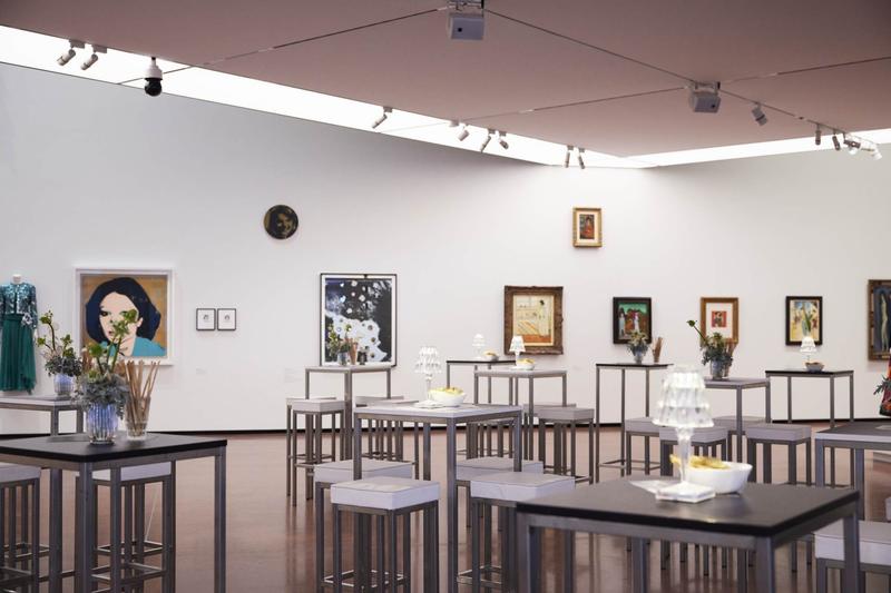 Moderne Galerie mit Tischen, Kunstwerken an Wänden und floralen Arrangements in Vasen.