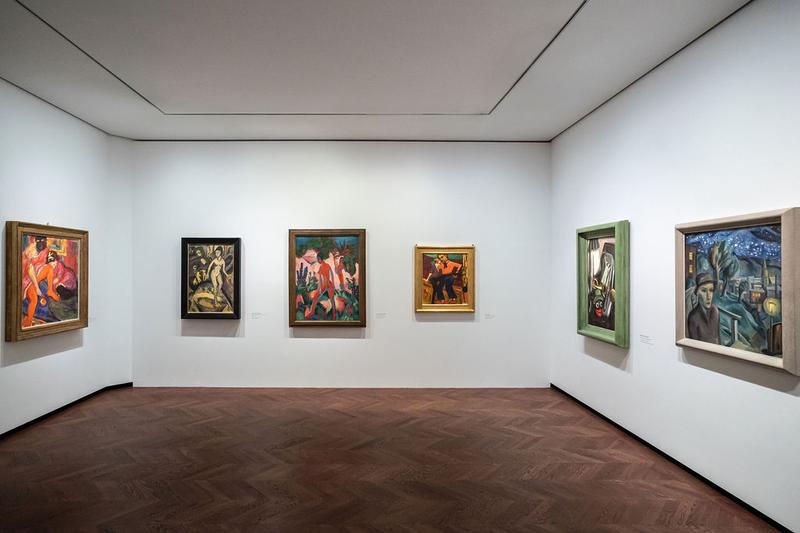 Auf dem Foto sieht man einen Raum aus der Ausstellung „Experiment Expressionismus“.
Der Raum ist hell, mit weiß gestrichenen Wänden und braunem Holzboden.

An den Wänden hängen sechs Gemälde.
Die Bilder zeigen Menschen in Bewegung, nackte Körper, starke Farben und besondere Posen – typisch für den Expressionismus.