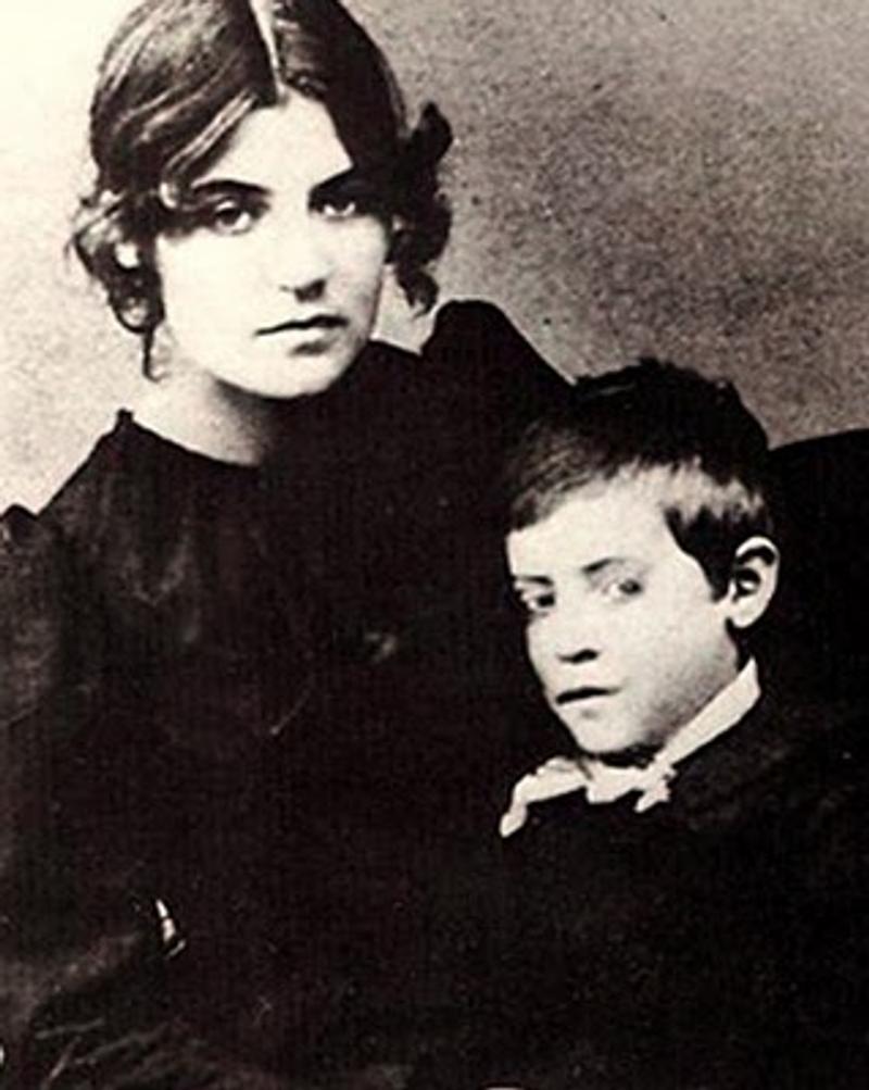 Suzanne Valadon sitzt mit ihrem Sohn Maurice Utrillo, beide in historischen Kleidern, ernst blickend in die Kamera.