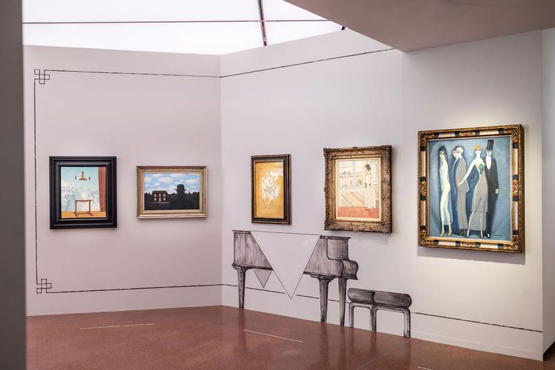 Auf dem Foto sieht man einen Teil der Ausstellung "Klimt⇄Warhol" im Museum der Heidi Horten Collection in Wien.

Man sieht eine Wand mit mehreren Gemälden. Links sind zwei surrealistische Bilder von René Magritte. 
Unter den Gemälde mittig befindet sich eine Verzierung in Form eines Flügels. Die Verzierungen an den Wänden und die gemalten Möbelstücke hat der Künstler Markus Schinwald gestaltet.