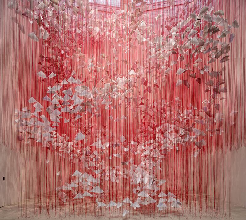 Die Installation füllt einen Ausstellungsraum mit einem dichten Geflecht aus leuchtend roten Fäden, die von der Decke bis zum Boden gespannt sind. Innerhalb dieses Netzes schweben hunderte weißer Papierbögen – sie wirken wie gefaltete Briefe, lose Blätter oder kleine Flügel. Die Briefe breiten sich wie in einer Luftbewegung spiralförmig nach oben oder außen auszubreiten. Die rote Farbe der Fäden dominiert den Raum. Die Fäden sind so zahlreich und dicht, dass sie aus der Ferne wie ein schimmernder Vorhang wirken, der die Grenzen des Raums verändert und ein begehbares, fast körperliches Erlebnis erzeugt.