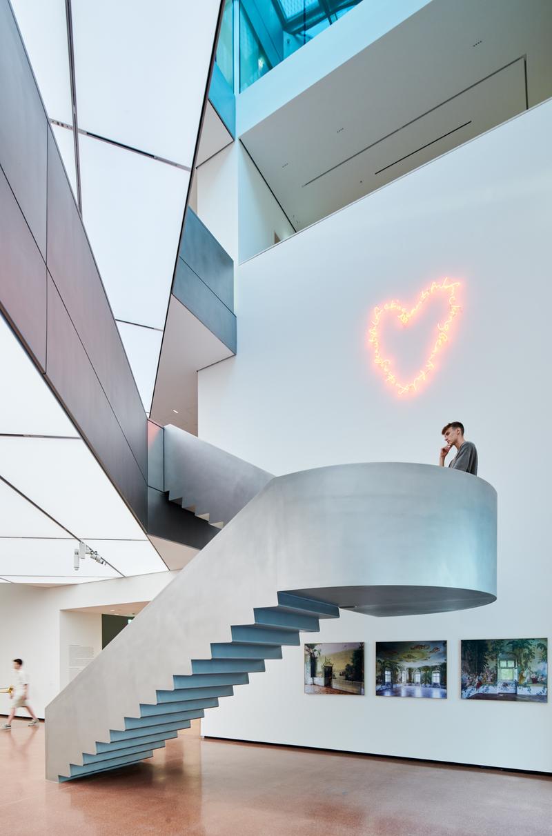 Moderne Treppe in einem hellen Raum, über der ein leuchtendes Herz-Symbol schwebt, mit Bildern an der Wand.