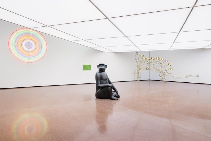 Schwarze Skulptur eines sitzenden Affen, bunte Lichtinstallation und goldene, tierähnliche Struktur in moderner Galerie.