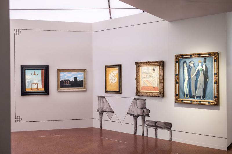 Auf dem Foto sieht man einen Teil der Ausstellung "Klimt⇄Warhol" im Museum der Heidi Horten Collection in Wien.

Man sieht eine Wand mit mehreren Gemälden. Links sind zwei surrealistische Bilder von René Magritte. 
Unter den Gemälde mittig befindet sich eine Verzierung in Form eines Flügels. Die Verzierungen an den Wänden und die gemalten Möbelstücke hat der Künstler Markus Schinwald gestaltet.