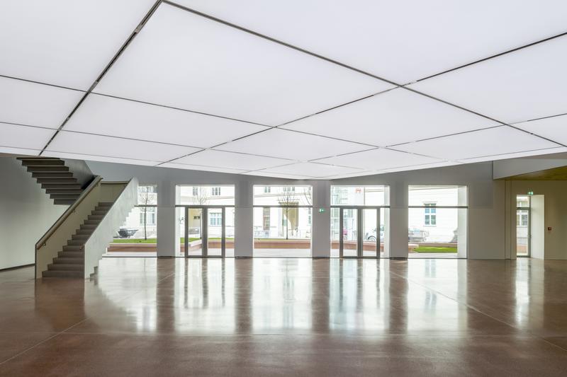 Heller, moderner Innenraum mit großen Fenstern, Treppe und glänzendem Boden.