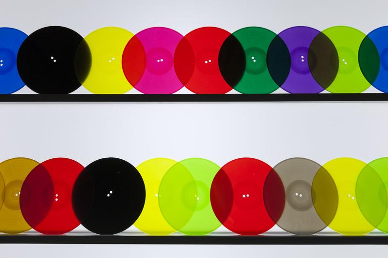 Bunte, transparente Platten in verschiedenen Farben auf zwei schwarzen Regalen angeordnet.