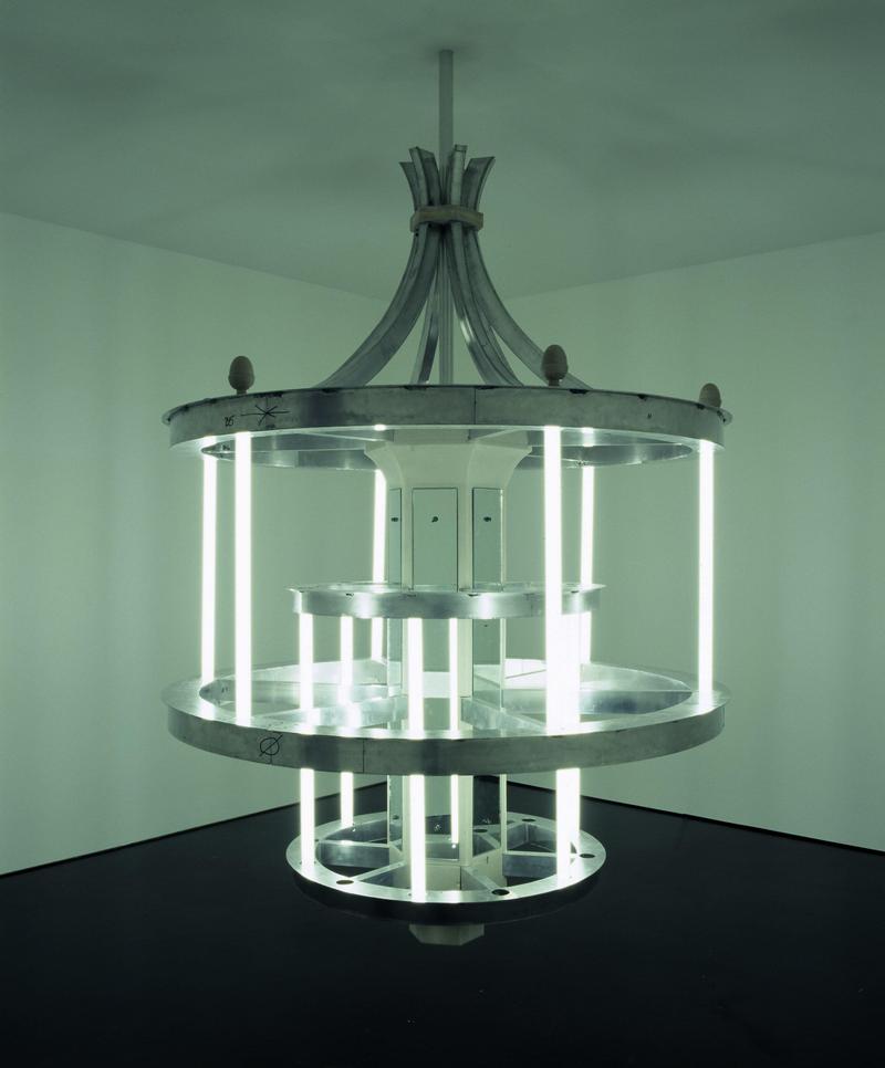 Hängende Lichtskulptur mit mehreren runden Ebenen und vertikalen Leuchtstoffröhren in einem minimalistischen Raum.